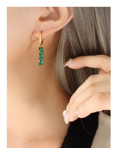 Detail of gold huggie earrings with three vertical square green zircons on a female model