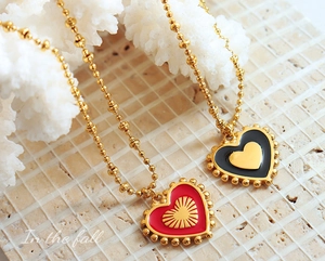 Detail view of red and black enamel heart pendants on a gold beaded chain necklace