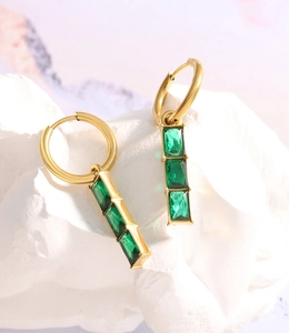 Macro shot of 18K gold plated hoop earrings with three square green zircons on white stone