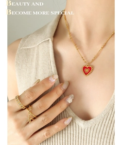 Detail of gold bead necklace with red enamel heart pendant and stacked rings on model