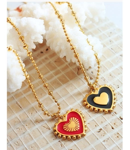 Macro detail of red and black enamel heart pendants with gold beaded chains on a textured surface
