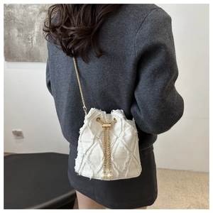 Detail of white quilted bucket bag with gold chain strap and pearl drawstring charms