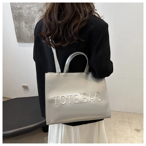 Detail of silver metallic tote bag with embossed letters worn by a model in a black blazer