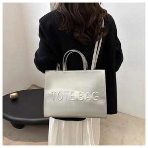 Detail of metallic silver tote bag with embossed lettering and glossy finish texture