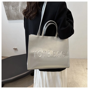 Silver metallic tote bag with embossed TOTE BAG text shown worn over the shoulder