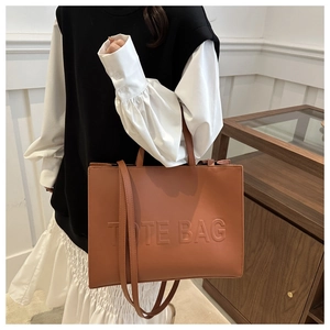 Close-up of caramel leather tote bag showing embossed lettering and textured matte finish