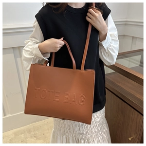 Brown textured leather tote bag with embossed letters shown on a female model