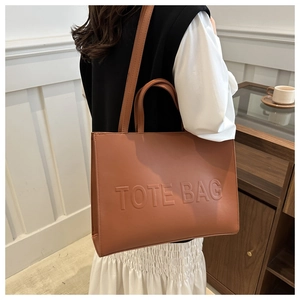 Brown leather tote bag featuring embossed TOTE BAG lettering and long shoulder strap