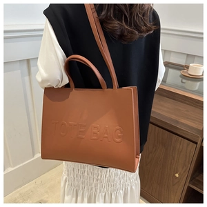 Detail of brown leather tote bag with embossed lettering and adjustable shoulder strap