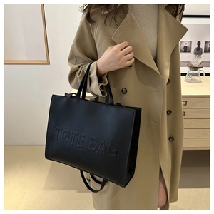 Detail of black matte leather tote bag featuring embossed lettering on the front