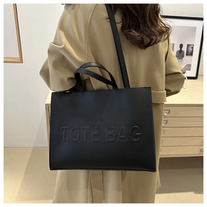 Close-up of embossed TOTE BAG text on textured black leather large commuter bag
