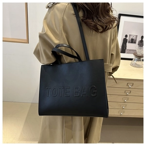 Detail of black leather tote bag with embossed lettering and dual strap functionality