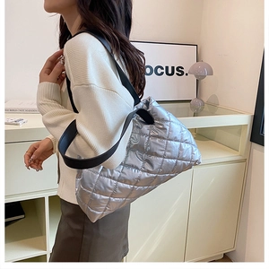Silver quilted metallic shoulder bag with black wide strap shown on model's shoulder