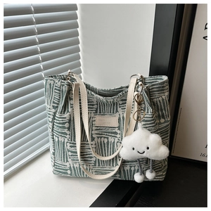 Detail of green striped canvas tote bag with plush cloud charm and leather brand tag