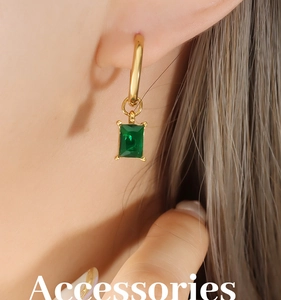 Close-up of elegant gold hoop earrings with emerald-cut green zircon drops on a model