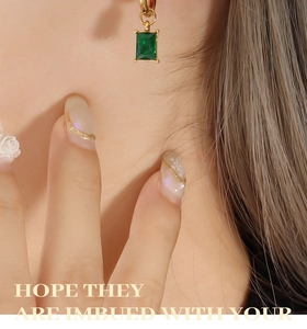 Detail of emerald green rectangular stone earrings with gold hoops on model
