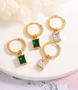 Close-up of gold hoop earrings with emerald green and clear crystal rectangle drops