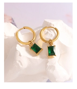 Close-up of golden hoop earrings with emerald green rectangular gemstone pendants