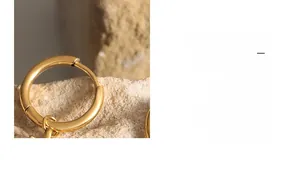 Macro shot of polished gold hoop earrings with small linked rings on a stone surface