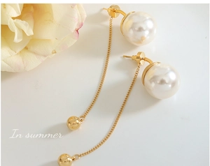 Détails de boucles d'oreilles pendantes dorées avec perles blanches sur fond épuré