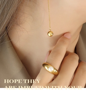 Gros plan sur une bague perle dorée et un collier pendentif boule polie sur modèle