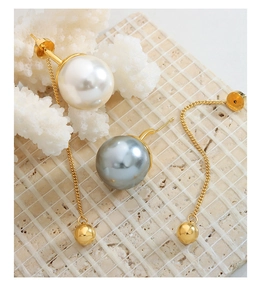 Détail de boucles d'oreilles chaînes dorées avec perles blanches et grises sur pierre