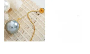 Détail macro d'une boucle d'oreille perle grise avec chaîne dorée sur pierre texturée