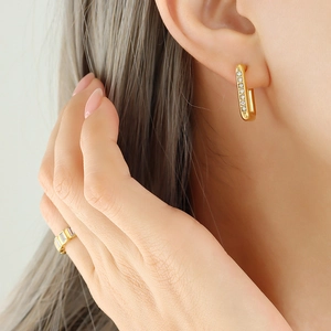 Orecchini geometrici placcati oro con zirconi chiari indossati da una modella