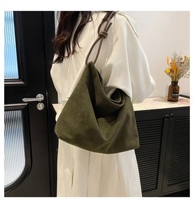 Close-up of deep green suede tote bag with brown knotted rope handles on a white coat