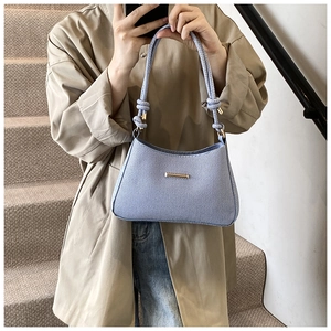 Detail of light blue denim saddle bag with woven handle and gold metal trim on model