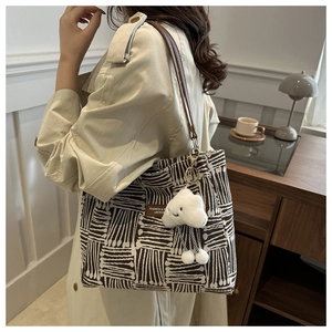 Detail of woven tote bag with brown leather straps and a cloud-shaped plush charm
