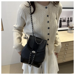 Detail of black leather crossbody bag featuring silver metal lock and woven chain strap