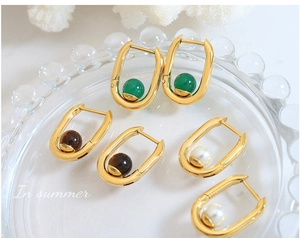 Détail de boucles d'oreilles dorées en U avec agate verte, oeil de tigre et perle
