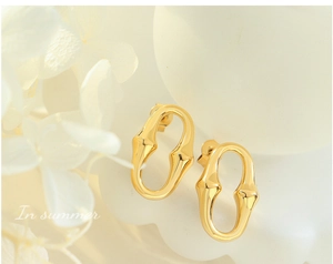 Détail de boucles d'oreilles dorées en forme de U avec texture bambou sur fond floral