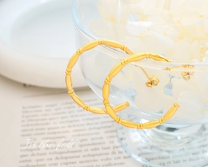 Detail of gold-plated bamboo-style C-shaped hoop earrings on a vintage paper background