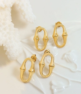 Détail macro de boucles d'oreilles ovales dorées avec nœuds texturés sur plateau céramique