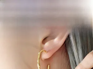 Macro view of gold bamboo texture C-shaped hoop earrings on a model's ear