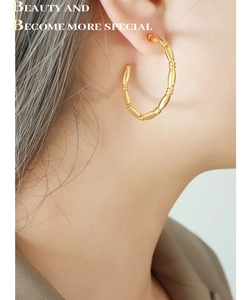 Close-up of golden bamboo-style C-shaped hoop earrings worn on a model's ear