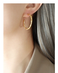Close-up of golden bamboo-textured C-shape earrings on a model with elegant matte finish