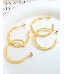 Macro detail of gold plated bamboo style C-shaped hoop earrings on a white ceramic plate