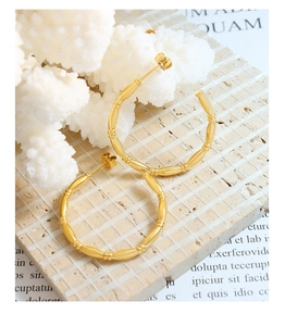 Detailed view of gold bamboo-textured C-shaped hoop earrings on a stone surface