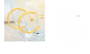 Detailed close-up of golden bamboo-textured C-shape earrings on a glass bowl rim