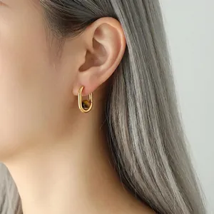 Boucles d'oreilles en U plaqué or avec perle oeil de tigre portées par un mannequin