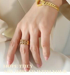 Close-up of gold chunky heart clasp Cuban bracelet and double-row chain ring on a model