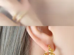 Detail of model wearing a twisted gold C-shaped hoop earring in polished stainless steel