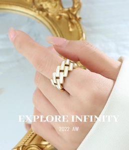 Détail d'une bague chaîne dorée avec émail blanc portée par un mannequin sous la lumière