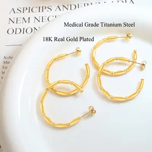 Bamboo style 18K gold plated titanium steel C-shape earrings on white ceramic plate