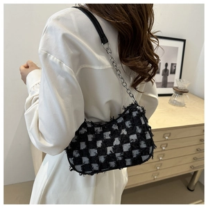Close-up of black and white checkered tweed underarm bag with frayed edges and silver chain