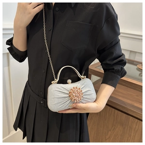 Pochette de soirée plissée argentée avec fleur en cristal et anse dorée sur robe noire