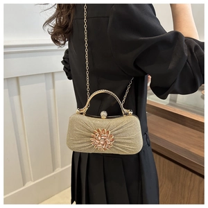 Pochette dorée avec fleur en strass portée par un mannequin en robe noire chic